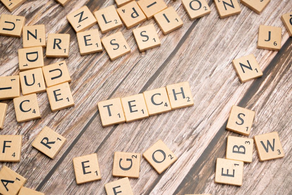Wooden Scrabble tiles spelling TECH on a textured surface, showcasing creativity.